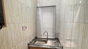 A compact kitchen with a sink, wooden cabinets, and a window with blinds.
