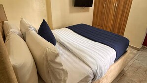 A bedroom with a bed, a TV mounted on the wall, and a wooden wardrobe.
