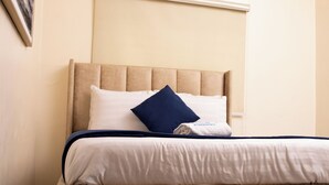 A neatly made bed with a headboard, white bedding, and a blue pillow.