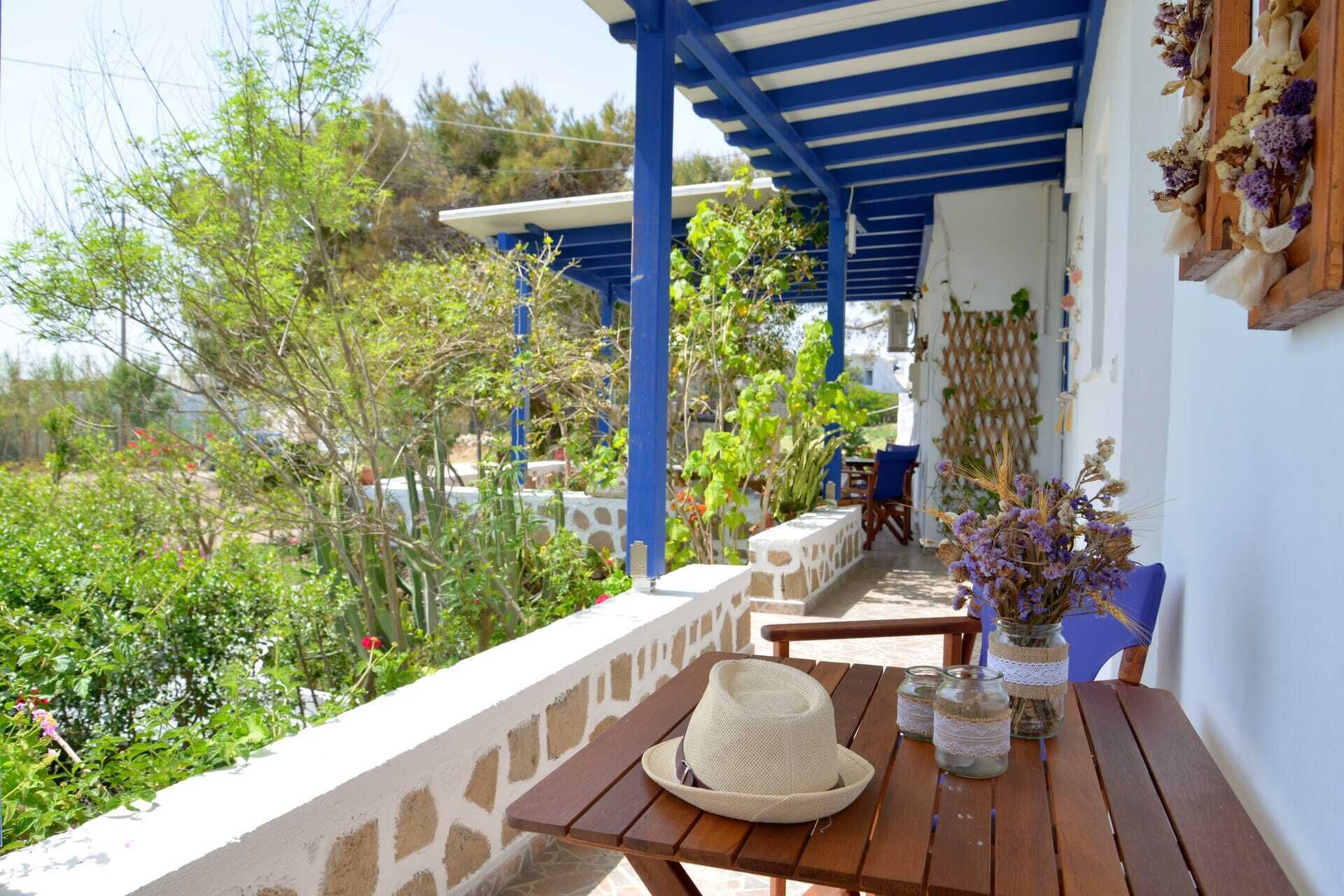 A wooden table with a straw hat and glass jars with lace, set on a balcony with a blue roof and white walls.