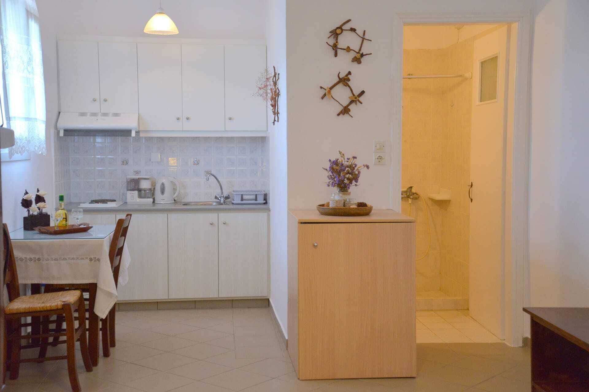 A compact kitchen with white cabinets, a dining table with chairs, a small wooden cabinet, and a shower area.