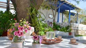 A table with glass jars containing flowers, a wooden tray with pottery, and a blue-roofed building in the background.