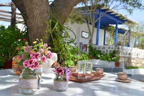 A table with glass jars containing flowers, a wooden tray with pottery, and a blue-roofed building in the background.