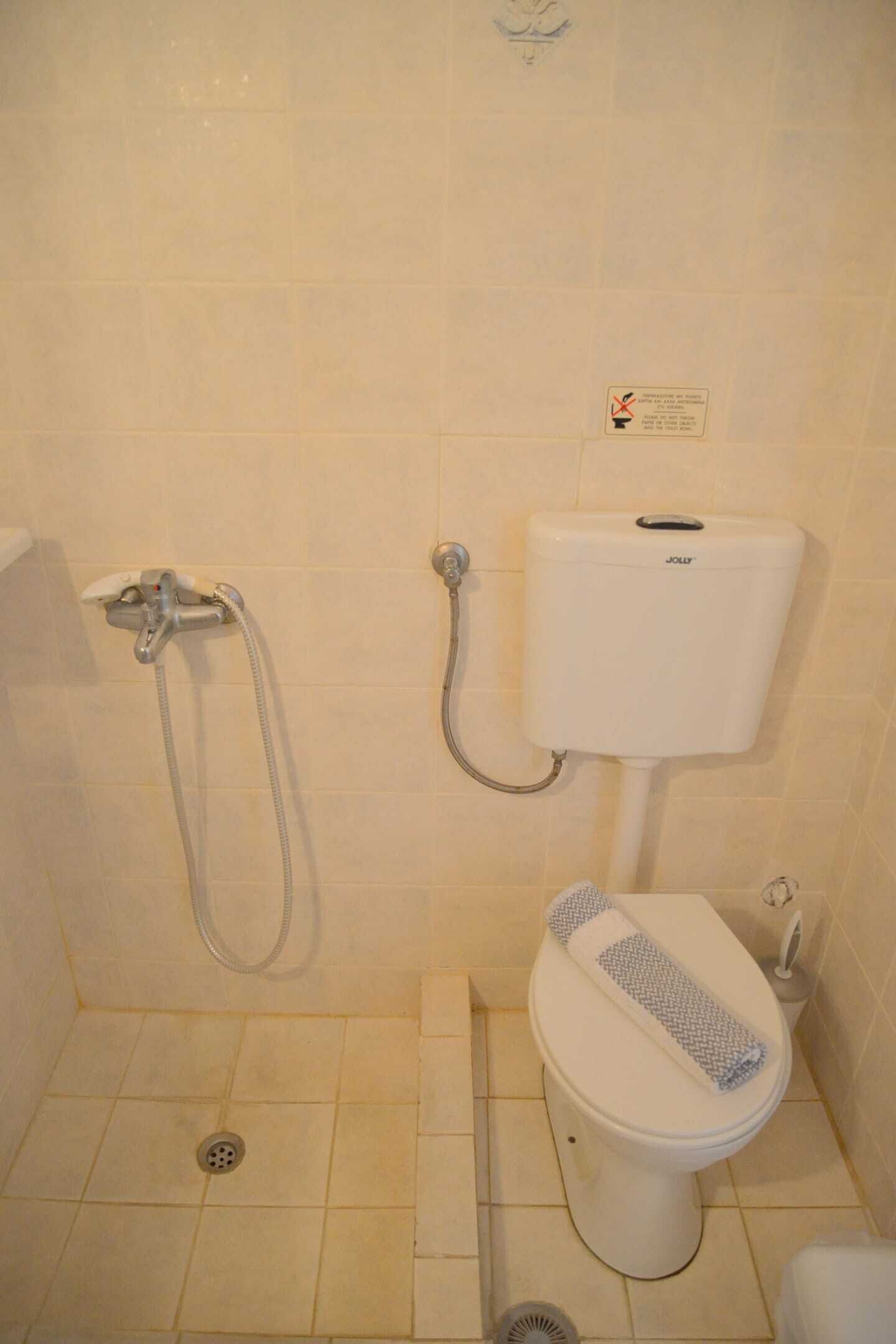 Et lille badeværelse med toilet, bruser og toiletpapirholder.