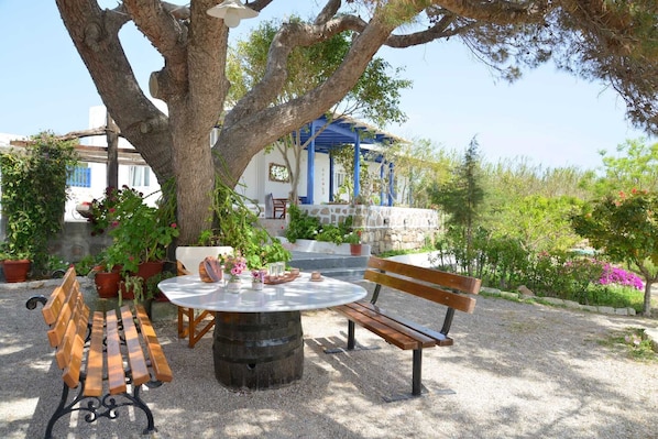 An outdoor seating area with a round table and benches, surrounded by potted plants and trees.