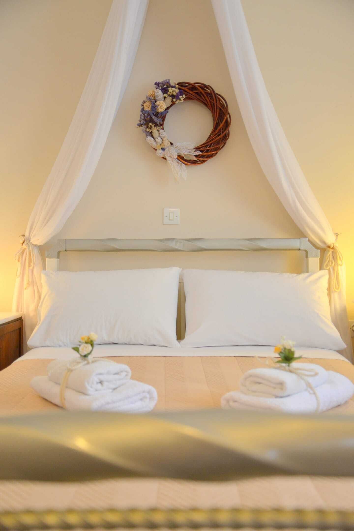A neatly made bed with white linens and a floral wreath on the headboard.