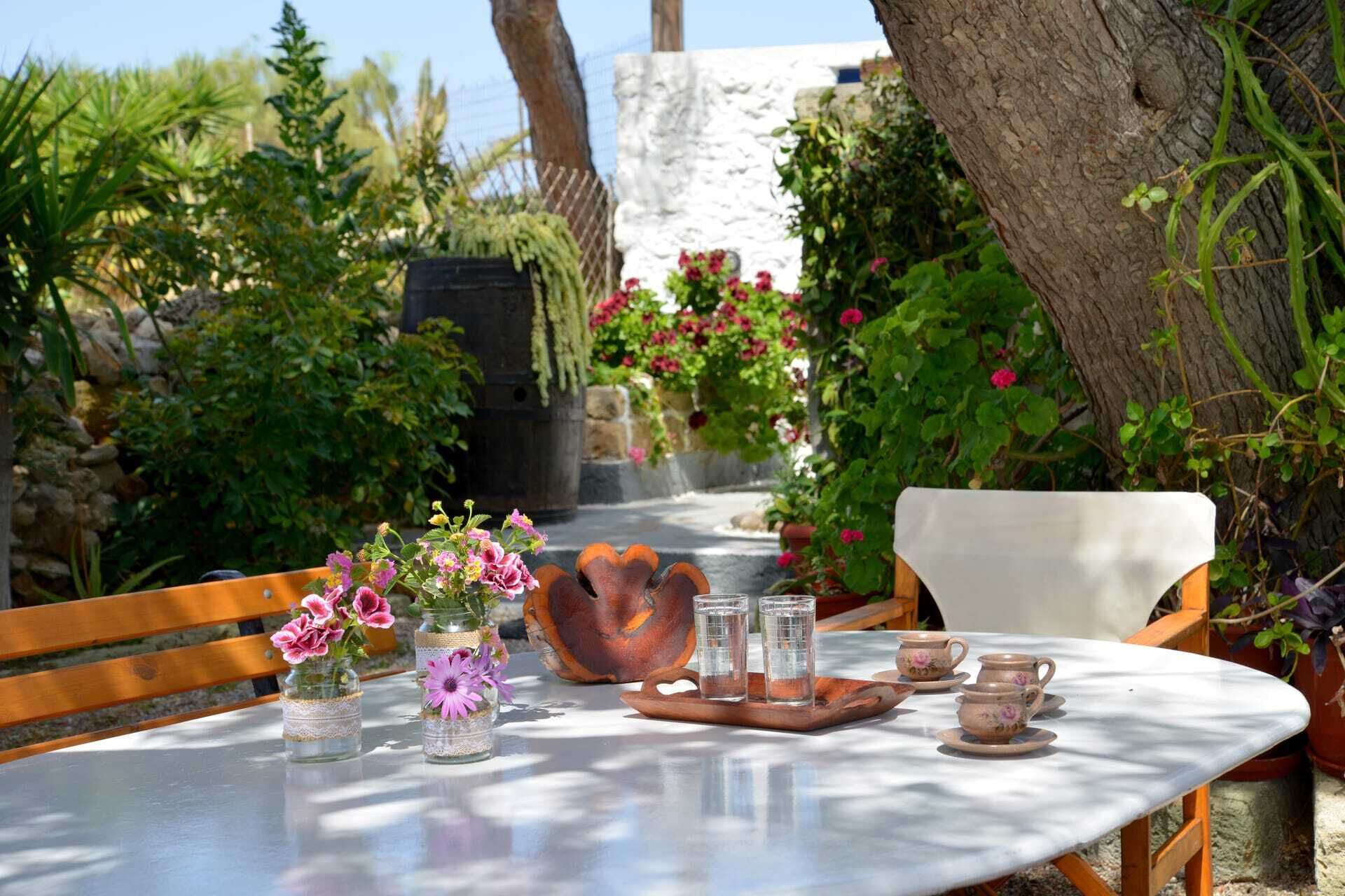 A table set outdoors with a rustic tablecloth, a wooden chair, and a variety of glass jars with flowers.