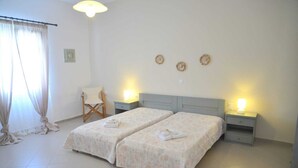 A hotel room with two beds, a chair, a nightstand, and a lamp. - Gemilos Nook Rooms II -  Double bed, Apartment (Milos)