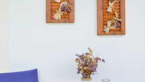 A wooden table with a vase of dried flowers, two wooden wall decorations, a blue chair, and a straw hat. - Gemilos Nook Rooms II -  Double bed, Apartment (Milos)