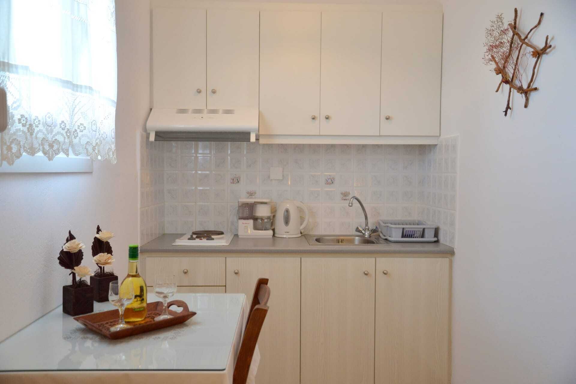 Cozinha com armários brancos, painel de azulejos, cafeteira, chaleira e bandeja com garrafa e copos.