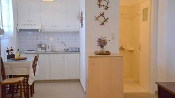 Een compacte keuken met witte kastjes, een eettafel met stoelen, een klein houten kastje en een douchegedeelte.