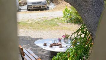 A table set outdoors with a bench nearby, surrounded by potted plants and a tree trunk.