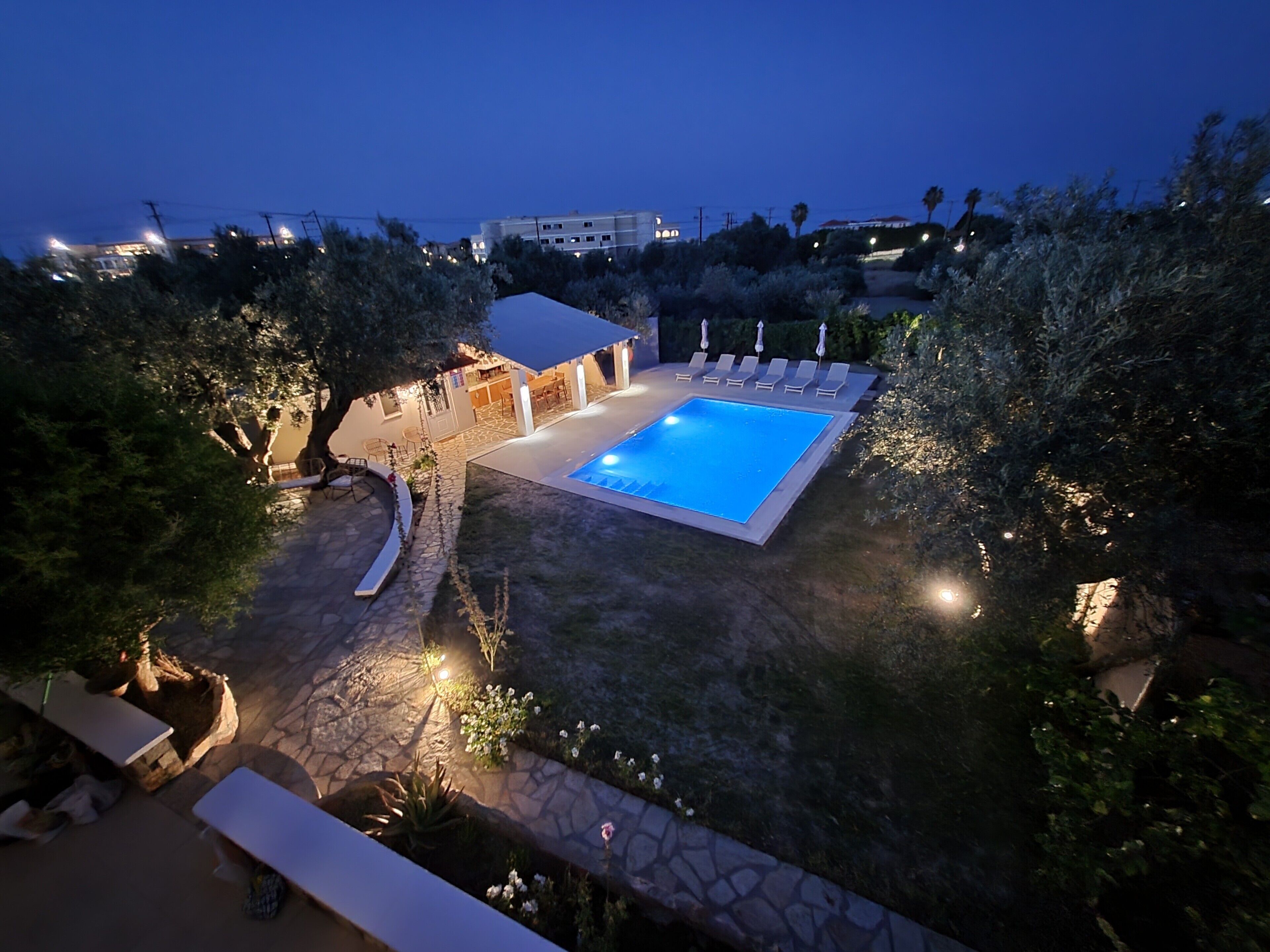 A swimming pool with a stone deck, surrounded by trees and a building with outdoor seating.