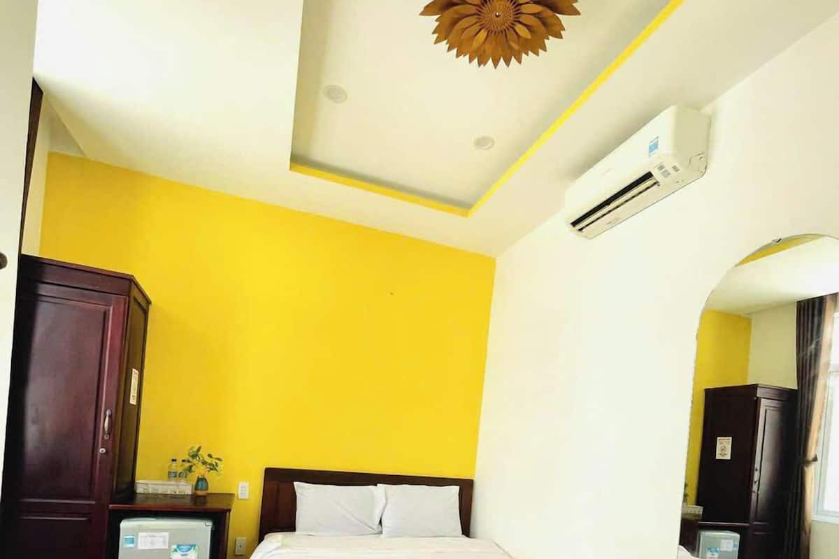 Une chambre d’hôtel avec un lit en bois, une petite table de chevet, un miroir et un mur d’accent jaune.