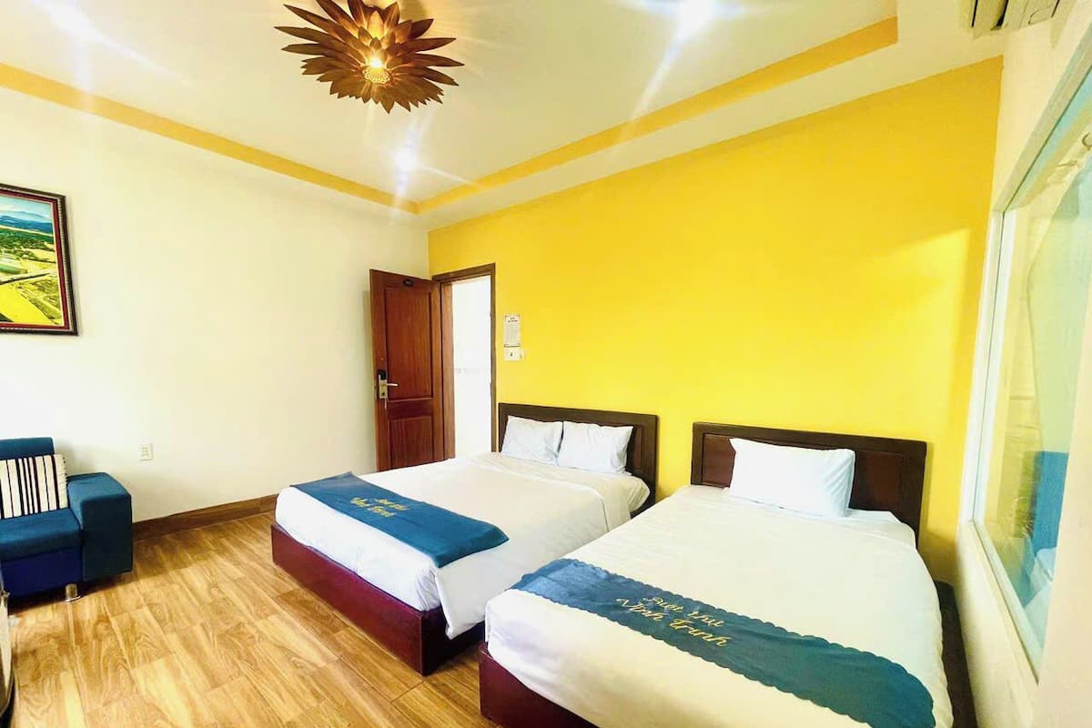 Une chambre d’hôtel avec deux lits, un plancher en bois, un mur jaune et un tableau encadré accroché au mur.