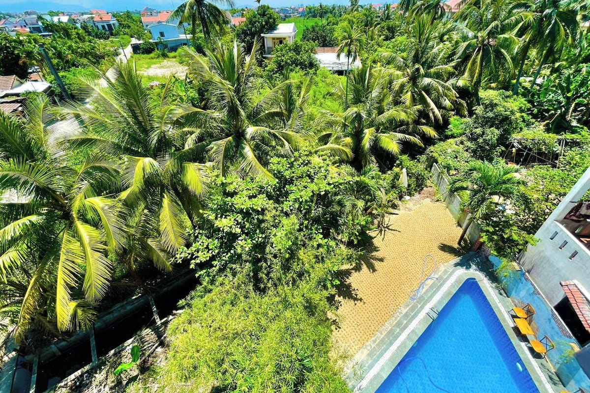 Un espace piscine offrant une vue dégagée sur le paysage environnant, notamment sur les palmiers et sur les habitations situées au loin.