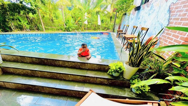 Una piscina con gradini che scendono verso l'acqua, circondata da vegetazione rigogliosa e un muro in mattoni.