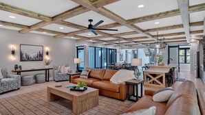 A spacious living room with a high ceiling, a ceiling fan, and a large window.