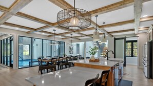 A spacious dining area with high ceilings and wooden beams, large windows, and a modern kitchen with stainless steel appliances.