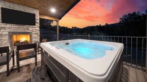 A hot tub on a deck with a stone fireplace and seating.