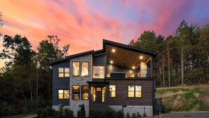 A modern two-story house with a stone facade, large windows, and a balcony.