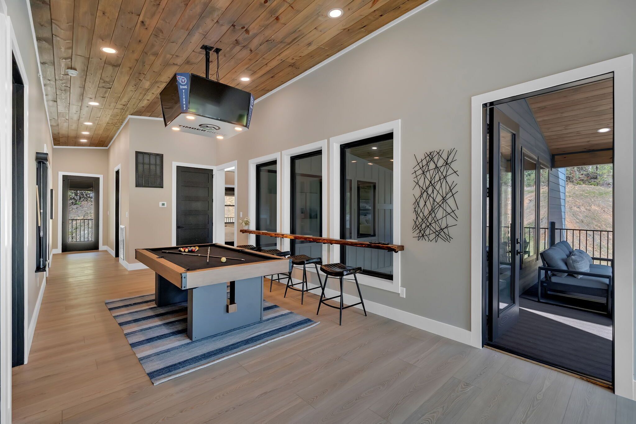 A modern indoor space with a pool table, bar stools, and a seating area with a view.