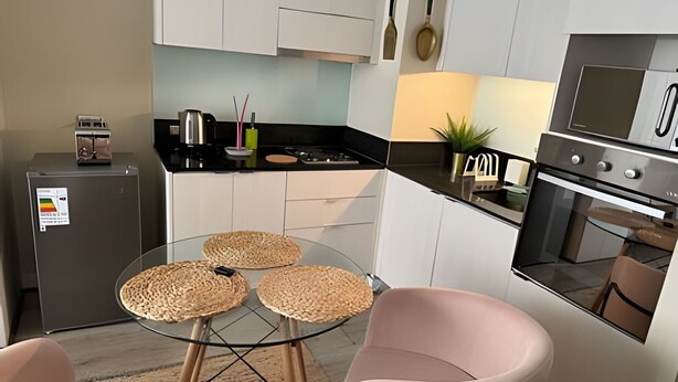 A modern kitchen with white cabinets, a black countertop, a glass table with woven placemats, and pink chairs. - Collection R 3 San Martin (Santiago)