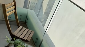 A corner seating area with two wooden chairs and a round table, a small potted plant, and a view of buildings through a window. - Collection R 3 San Martin (Santiago)