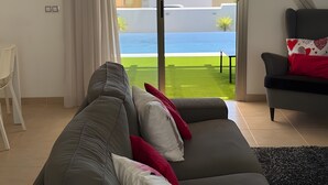 Ein Wohnzimmer mit einer Couch, einem Sessel und Blick auf eine grüne Wiese und Gebäude.