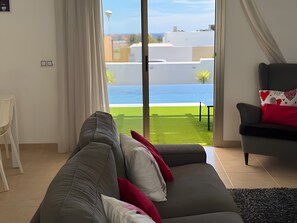 Un salon avec un canapé, un fauteuil et une vue sur une pelouse verdoyante et des bùtiments.