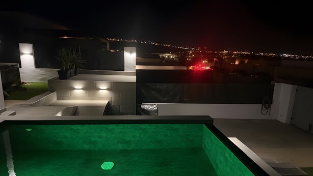 Ein Pool mit Stufen, umgeben von einer modernen Außenanlage mit Blick auf eine nächtliche Skyline.