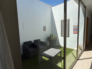 Un espace extérieur moderne aménagé avec des siÚges, un pot de fleurs, une petite table et un panneau fixé au mur.