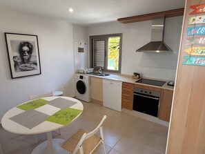 Une cuisine compacte équipée d’un lave-linge, d’un évier, d’une cuisinière et d’un coin repas avec une table et des chaises.