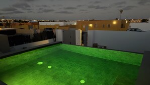 Ein Dachpool mit Kunstrasen und Blick auf die Stadt bei Dämmerung.