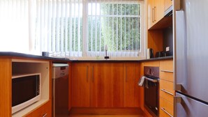 A kitchen with wooden cabinets, a stainless steel refrigerator, a built-in oven, and a window with blinds.