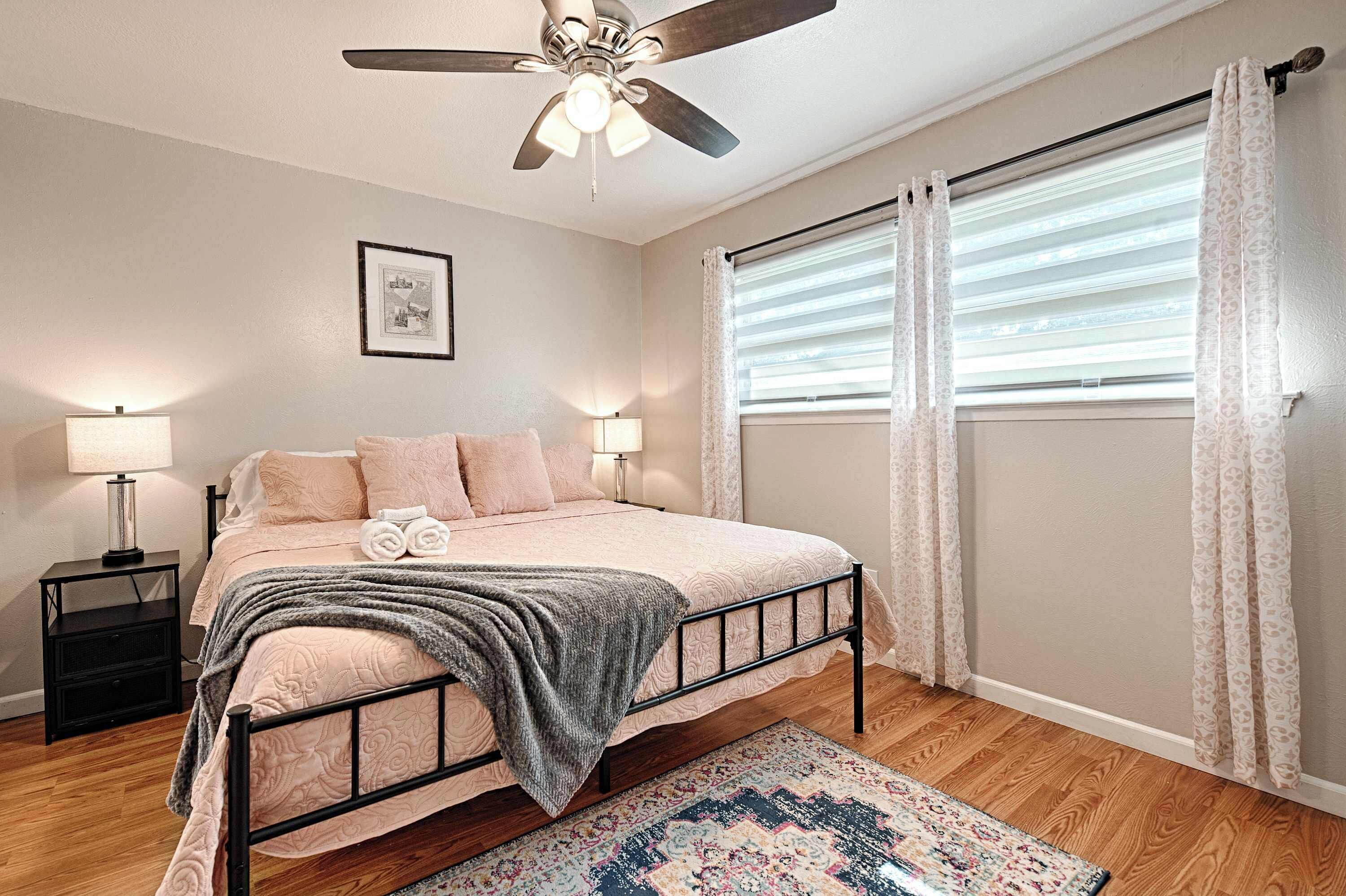 A bedroom with a bed, bedside lamps, a ceiling fan, a window with blinds, and a rug.
