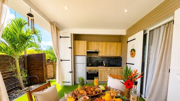A breakfast setup with tropical decor, a kitchen in the background, and a view of a palm tree.