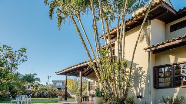 A house with a covered patio, a garden with palm trees, and a view of the surrounding area.