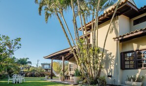 A house with a covered patio, a garden with palm trees, and a view of the surrounding area. - 3-bedroom House 800m From the Beach Tab0140 (Garopaba)