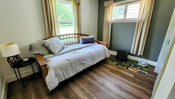 A bedroom with a wooden bed, a nightstand, a lamp, a window with curtains, and a small rug.