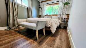 A bedroom with a bed, a chair, wooden flooring, a window with curtains, and a plant. - Meet Bev, a charming 2-bedroom, pet-friendly home in Rochester (Rochester)