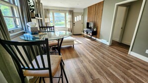A modern living room with a glass-top dining table, wooden flooring, and a TV stand with a flat-screen TV. - Meet Bev, a charming 2-bedroom, pet-friendly home in Rochester (Rochester)