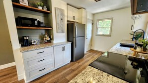A modern kitchen with white cabinets, a stainless steel refrigerator, a granite countertop, and a black stove. - Meet Bev, a charming 2-bedroom, pet-friendly home in Rochester (Rochester)
