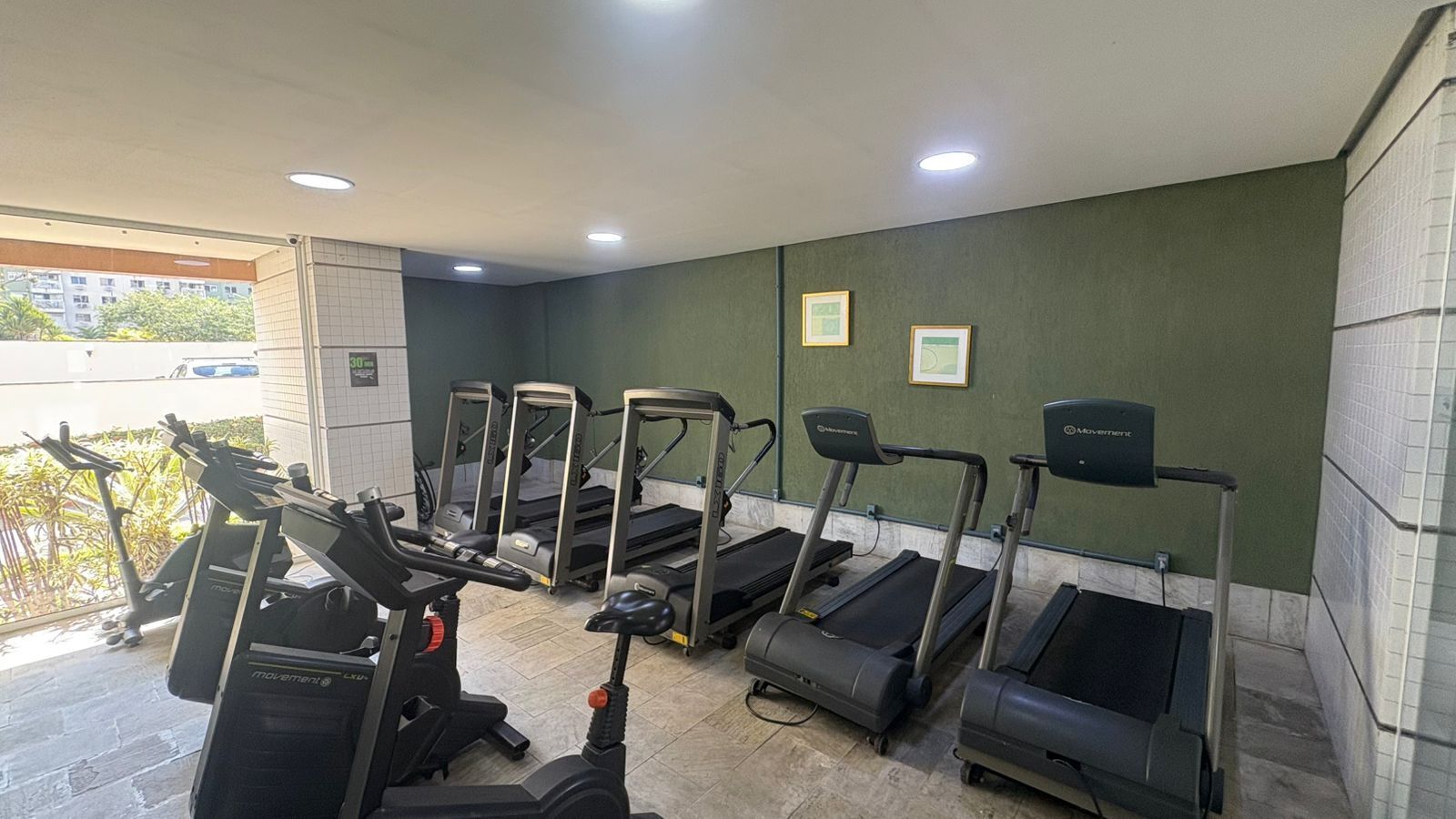 Et fitnesscenter med løbebånd og crosstrainere, grønne vægge og et flisegulv.