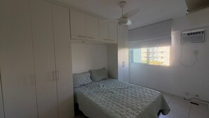 A bedroom with a bed, a wardrobe, a ceiling fan, a window, and an air conditioning unit. - Barra Olímpica Riocentro Apartment (Camorim Rio de Janeiro)