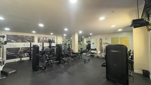 A gym with various exercise equipment, mirrors, and a clock on the wall. - Barra Olímpica Riocentro Apartment (Camorim Rio de Janeiro)