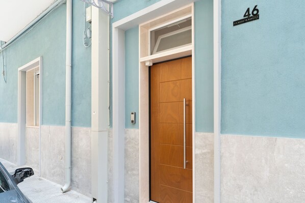 A building with two doors, one with a wooden panel and the other with a glass panel. There is a number '46' on the wall and a small sign above the door.