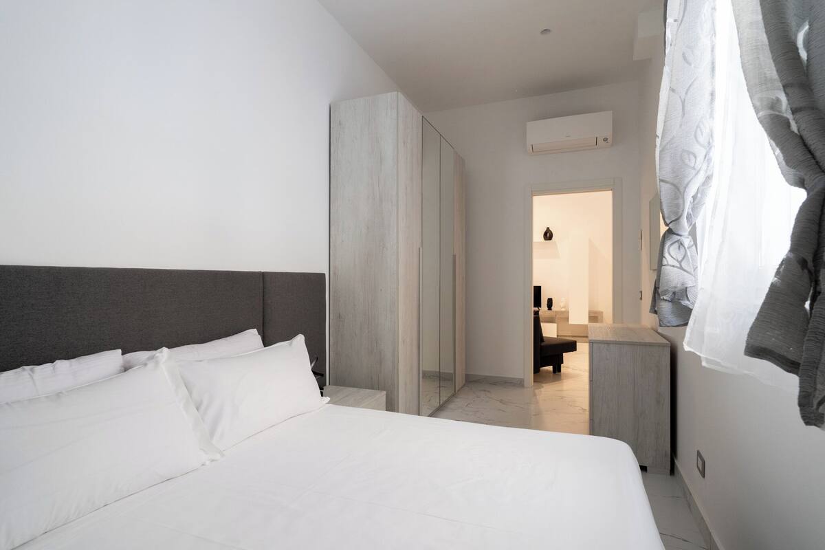 Een moderne hotelkamer met een groot bed, een kledingkast en een badkamer zichtbaar door een geopende deur.