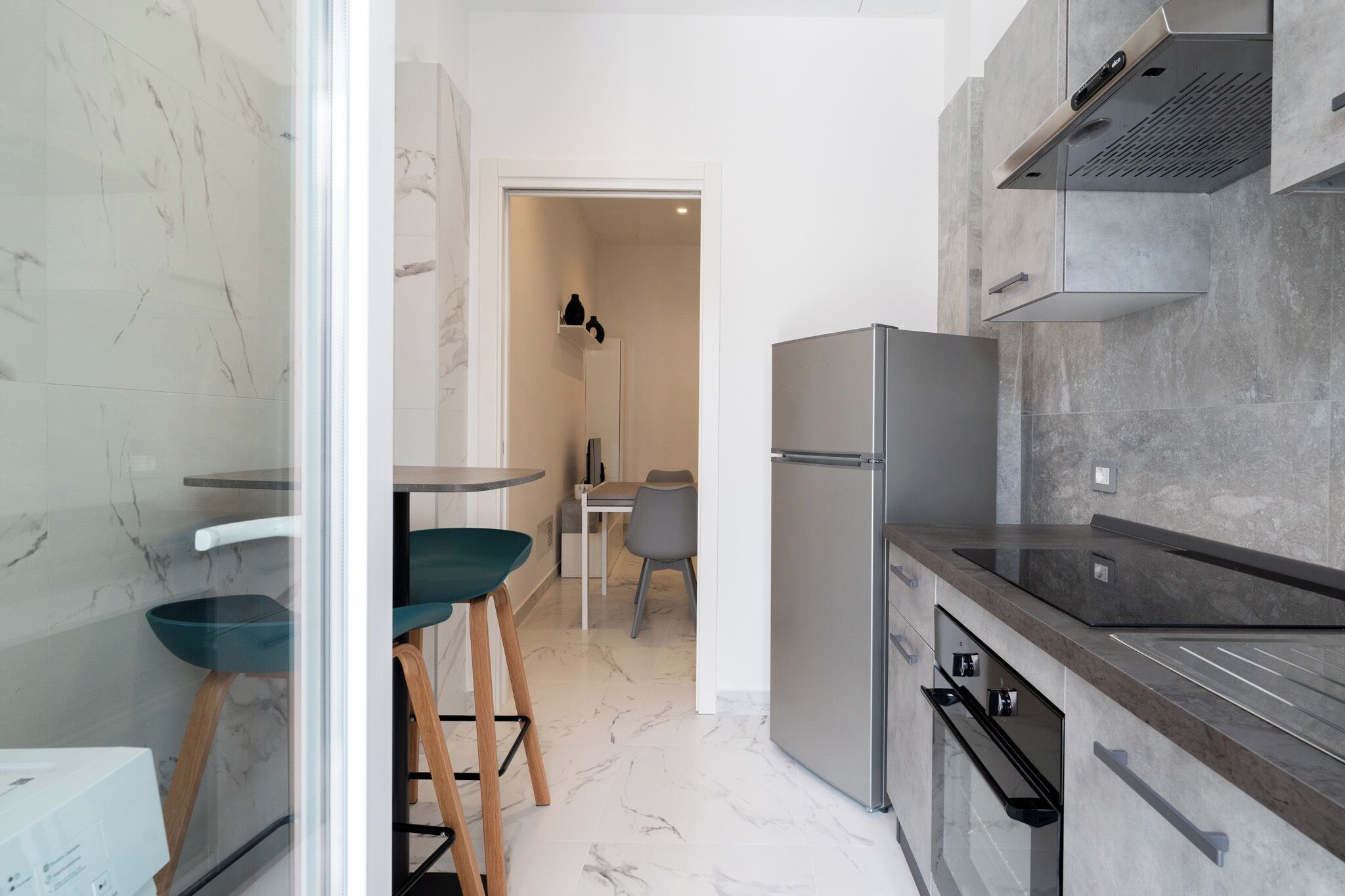 Une cuisine moderne dotée d’un réfrigérateur en acier inoxydable, d’un four encastré et d’un plan de travail élégant. On y trouve deux tabourets et une table avec des chaises.