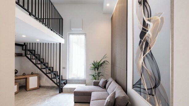 A modern living room with a staircase, a large abstract painting, and a potted plant.
